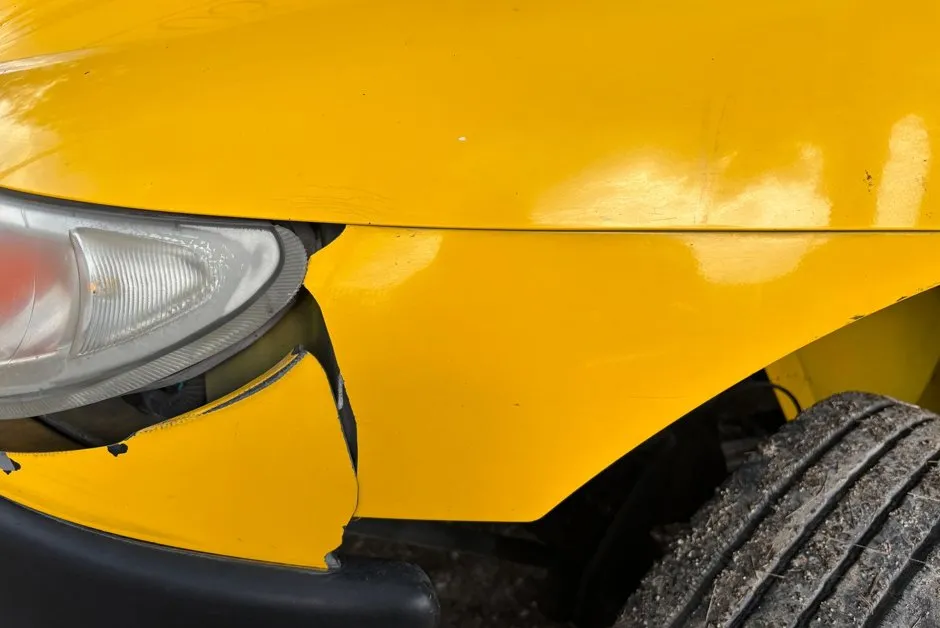 Petit stylo de retouche peinture appliqué sur un éclat de carrosserie rouge sur une portière de voiture